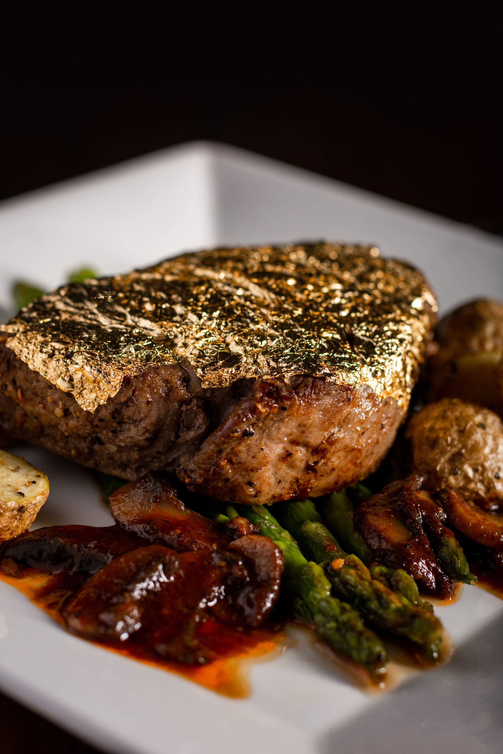Gold-encrusted steak plated with roasted potatoes and asparagus, captured inside Tarbenders Lounge’s speakeasy.