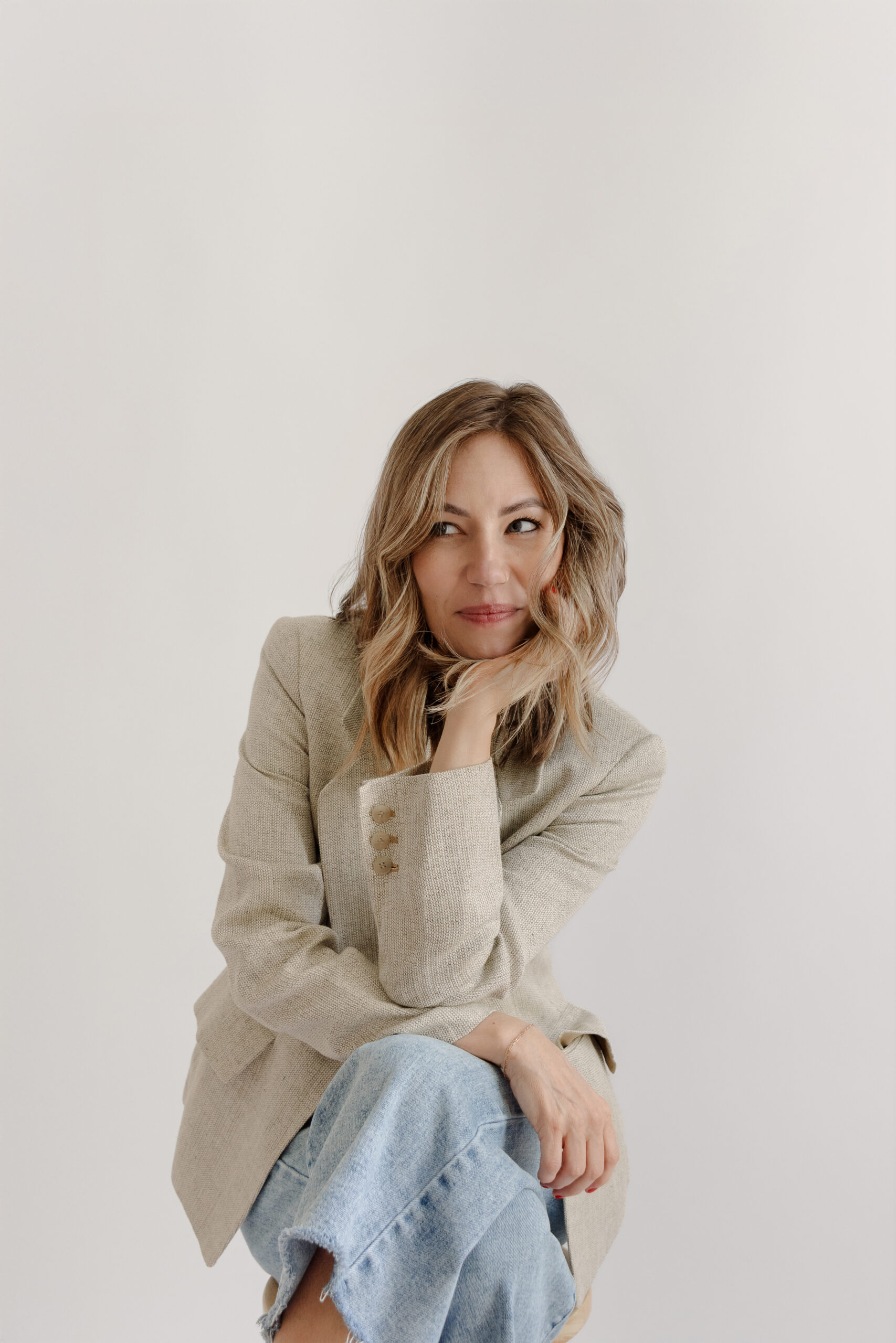 Ali, founder of Everroot Holistic Psychotherapy, seated in a soft beige blazer and denim, photographed in a modern studio for her branding session